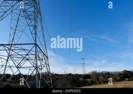 High voltage towers with electricity transmission power lines in field on sunny day Stock Photo