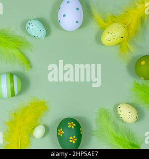Beautiful festive Easter frame made of colored eggs, feathers on a green background. Copy space for your design. View from above. Place for text. Stock Photo