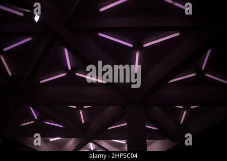 Purple glow of lamps. Fluorescent lamps shine in dark. Background of triangular lamps. Texture of bright streaks in dark. Stock Photo