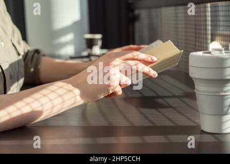 Hands closeup holding book. Woman sitting at cafe table and reading book. Reading literature hobby concept . High quality photo Stock Photo