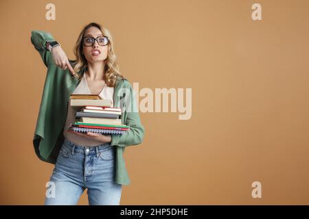 Serious young woman in glasses pointing finger at a pile of books in her hands isolated over gray background Stock Photo