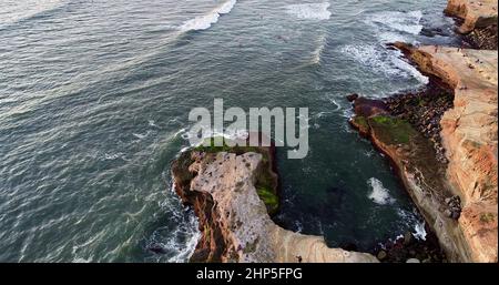 Aerial view of people watching golden sunset at Sunset Cliffs Natural Park while waves crash on rocks, San Diego, California, USA Stock Photo