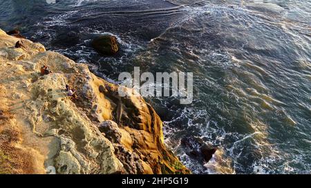 Aerial view of people watching golden sunset at Sunset Cliffs Natural Park while waves crash on rocks, San Diego, California, USA Stock Photo