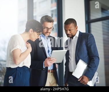 Shared knowledge benefits everyone in business. Shot of a team of colleagues using a digital tablet together at work. Stock Photo