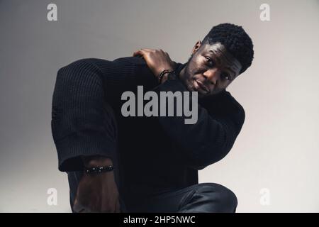 stressed person of color touching his shoulder seated white background - medium shot. High-quality photo Stock Photo