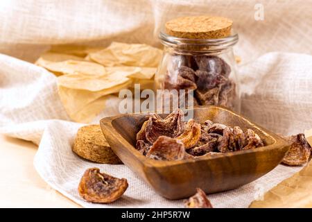 Traditional Japanese hoshigaki dried persimmon fruit snack slices in wooden bowl and glass jars on light background. Stock Photo