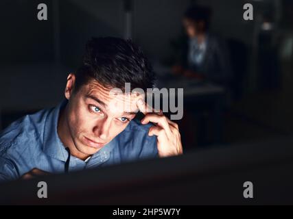 Working the late night grind to get the work done. Cropped shot of a young attractive businessman working late in the office. Stock Photo