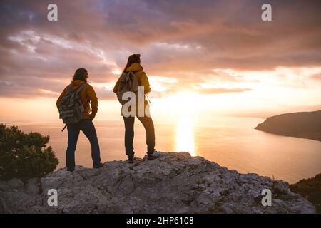 Two hikers with backpacks looks at sea sunset from view point Stock Photo