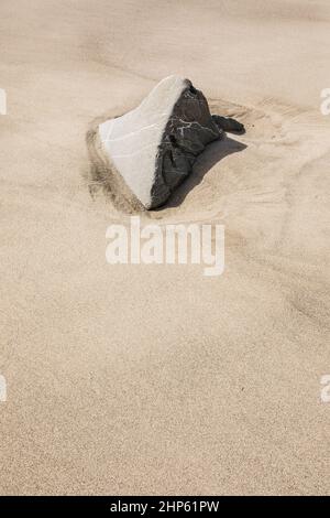 A rock exposed above a sandy beach after tides have receded. Stock Photo