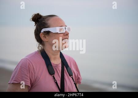 A woman views the partial solar eclipse as the sun rises, Thursday, June 10, 2021, at Lewes Beach in Delaware. The annular or “ring of fire” solar eclipse is only visible to some parts of Greenland, Northern Russia, and Canada. Stock Photo