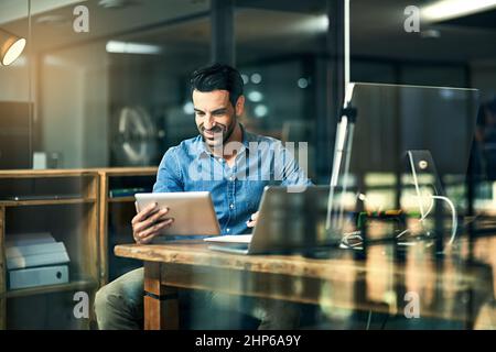 Technology - An entrepreneurs best friend. Shot of a young businessman using a digital tablet during a late night at work. Stock Photo