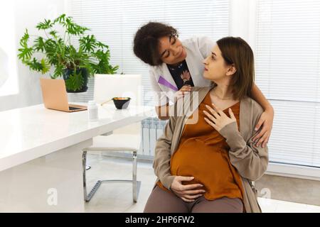 Young happy grateful woman patient hugging with friendly positive African-American female doctor after receiving good test results or recovery during Stock Photo