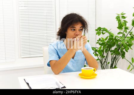 Tired depressed african american woman doctor or nurse in uniform suffer from headache after hard working day or sleepless night shift in clinic, sitt Stock Photo
