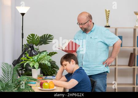 Dad reads a book and helps his son with his school assignment. Stock Photo