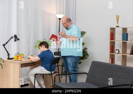 Dad reads a book and helps his son with his school assignment. Stock Photo