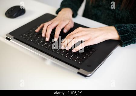 Freelancer woman typing on computer keyboard. Businesswoman working on modern laptop. Hands of white female doing work on notebook pc at home during l Stock Photo