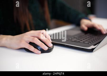 Freelancer woman clicking with wireless mouse. Entrepreneur female working on modern laptop computer at home. Businesswoman doing distant work online Stock Photo