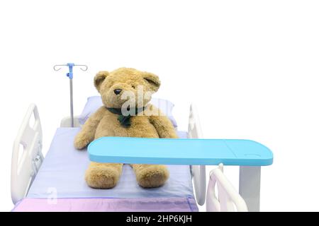 rown teddy bear lying sick in bed with overbed table on body, isolated on white background, medical and healthcare concept Stock Photo