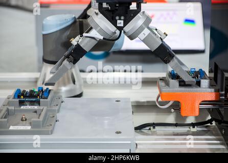 Close-up industrial gripping robot working with electronic circuit board put on pass tray by automation system via setting work program, industry 4.0 Stock Photo