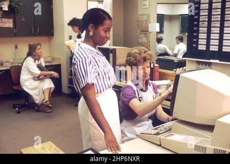 Several nurses in a nurses' station, two of which are working on a computer accessing PDQ. Physicians Data Query was designed by the National Cancer Institute to help physicians and patients obtain information on protocols, physician referrals and clinics using the most up-to-date cancer treatments. ca.  June 1987 Stock Photo