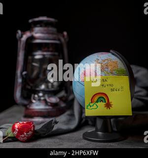 A sticky note that says "everything will be fine" in Italian, attached to a small globe with a vintage lantern in the background Stock Photo