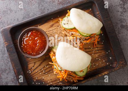 Pulled pork in a Bao roll served with sauce closeup in the wooden board on the table. Horizontal top view from above Stock Photo