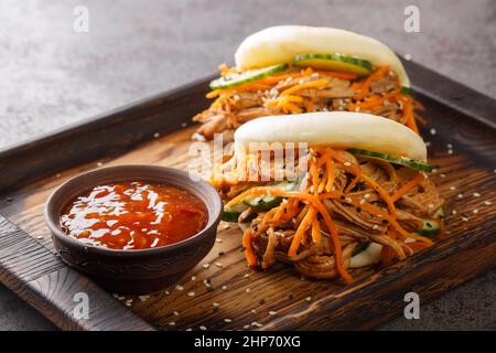 Pulled pork in a Bao roll served with sauce closeup in the wooden board on the table. Horizontal Stock Photo