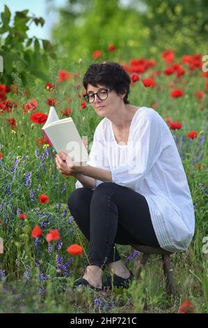 Woman In A Poppy Field Reading and Holding A Book Stock Photo
