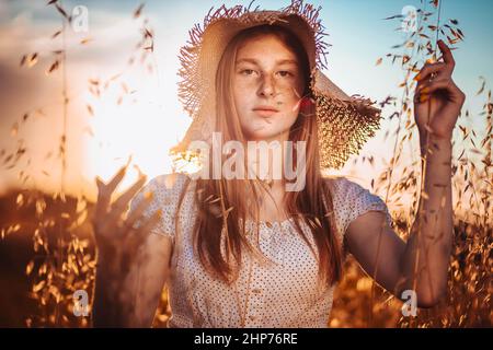 Portrait of young, teen, ginger girl with freckles in the wheat field wearing a summer hat Stock Photo