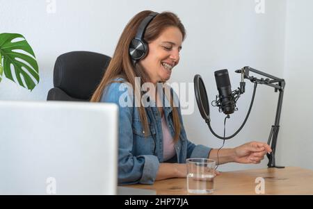 Mature woman recording a podcast using microphone and laptop from her home studio Stock Photo