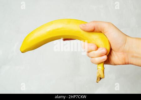 Female hand holding a fresh ripe banana against a neutral background. Stock Photo