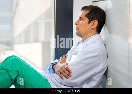 Cropped shot of an handsome young male doctor looking exhausted while leaning against a wall in her hospital Stock Photo