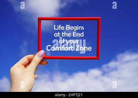 Life begins at the end of your Comfort Zone. Red frame in a female hand against the blue sky. Go beyond thinking. Motivational concept Stock Photo