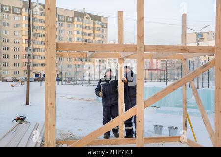 A builder in a blue jacket with a hammer in his hand hammers a nail Stock Photo