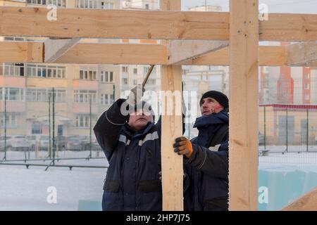 A builder in a blue jacket with a hammer in his hand hammers a nail Stock Photo