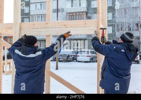 A builder in a blue jacket with a hammer in his hand hammers a nail Stock Photo