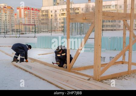 A builder in a blue jacket with a hammer in his hand hammers a nail Stock Photo