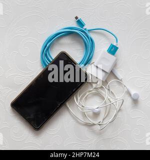 Flatlay phone, charger, headphones on white table Stock Photo