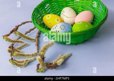 Easter egg as a decoration in a green basket. Decorated Easter eggs on the Easter table. The background is bright. Next to the basket is a willow twig Stock Photo