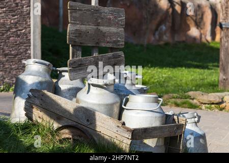 Old metal milk jugs on a wooden cart by the road. Stock Photo