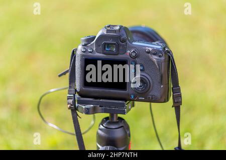 Rear view of a digital camera. The display and rear controls are visible. The camera is mounted on a tripod. The background is green. Stock Photo