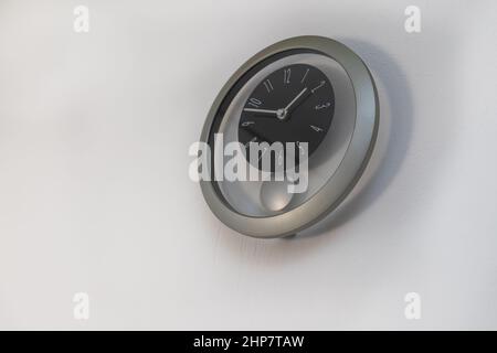 A round wall clock with a pendulum is mounted on a white wall. Stock Photo