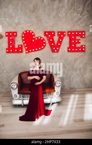 Charming pregnant woman in marsala dress posing on steps of house. Stock Photo