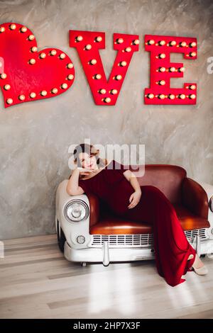 Charming pregnant woman in marsala dress posing on steps of house. Stock Photo
