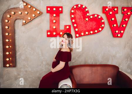 Charming pregnant woman in marsala dress posing on steps of house. Stock Photo