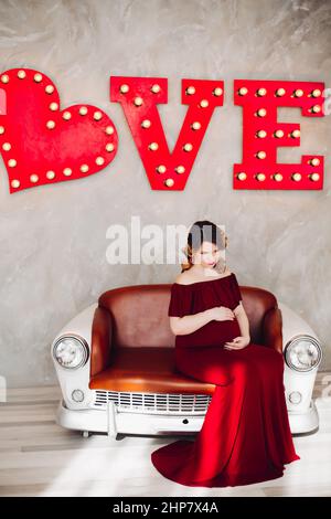 Charming pregnant woman in marsala dress posing on steps of house. Stock Photo