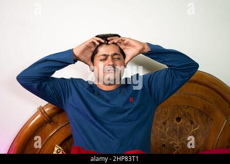 young man holding head due to headache or migraine at bedroom - concept of Healthcare, Stock Photo