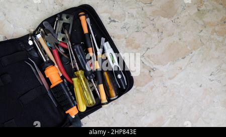 A tool bag with unsorted tools of tweezers, screwdrivers, pliers, and others. Placed on a marble surface with copy space on the right. Stock Photo