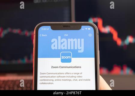 Zoom Communications stock price decrease on the trading market with downtrend line graph bar chart on the background. Man holding a mobile phone with company logo, February 2022, San Francisco, USA.  Stock Photo