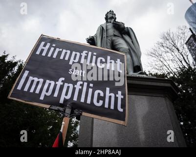 19 February 2022, Hessen, Frankfurt/Main: A participant holds a placard reading 'Hirnpflicht statt Impfpflicht' (compulsory brain instead of compulsory vaccination) under the monument to the poet Friedrich Schiller during a demonstration of several thousand people against corona measures and compulsory vaccination in downtown Frankfurt. Photo: Frank Rumpenhorst/dpa Stock Photo